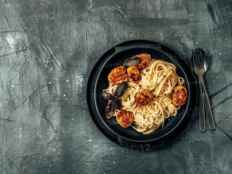 Zucchini Parmesan Meatballs with Pasta Carbonara in black craft plate over gray background. Close up view of creamy carbonara with copy space left. Top view or flat lay