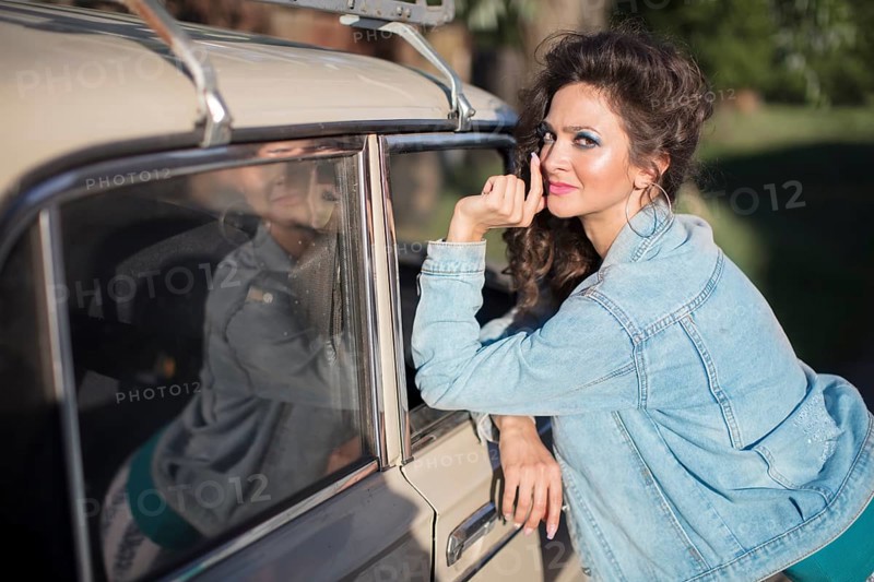 Funny young woman in a denim jacket with light-coloured make-up on the background of an old car