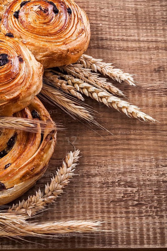 Ripe wheat ears rich rolls with raisins on oaken wooden board food and drink concept