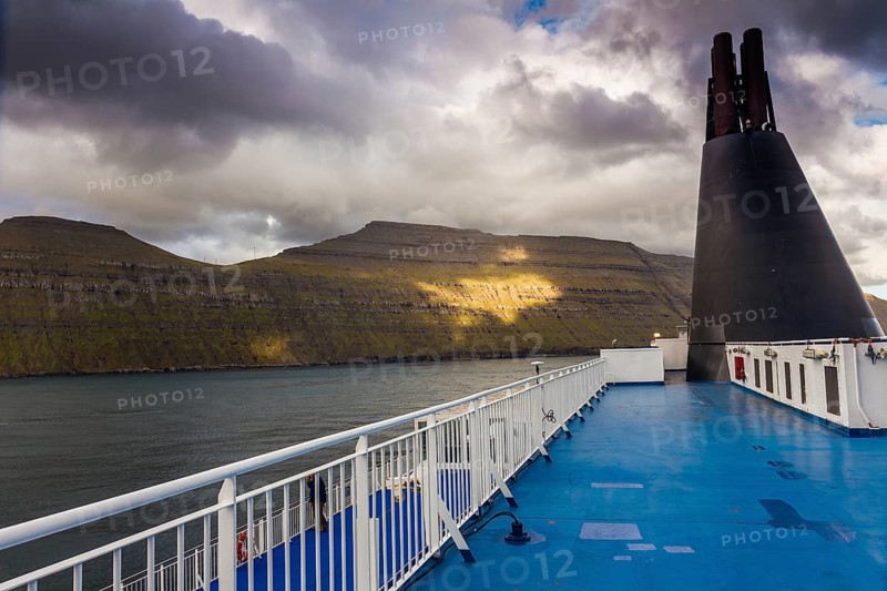 Blue sun deck of a ferry with the coast of the Faroe Islands in the background