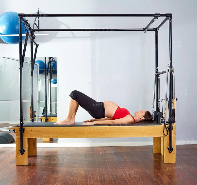 Pregnant woman pilates reformer shoulder bridge exercise workout at gym