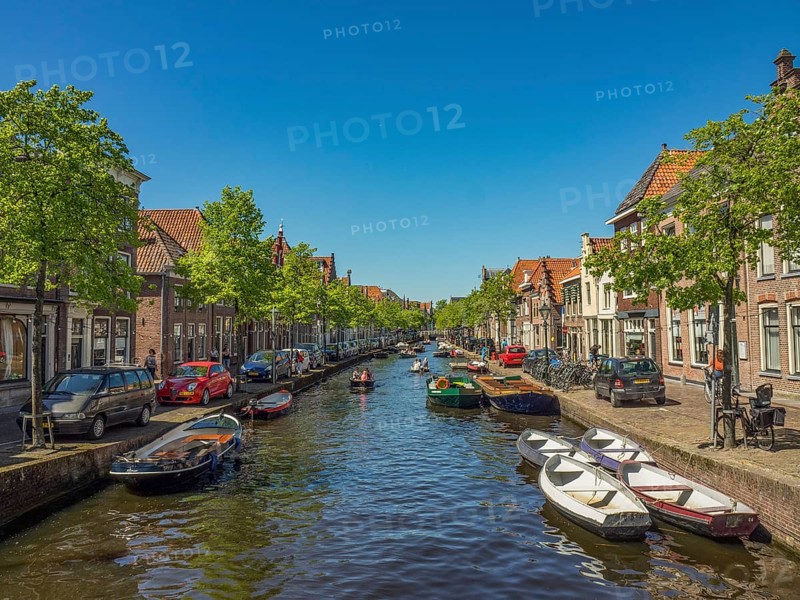 A long canal lined with boats, cars and historic buildings on a sunny day, alkmaar, the netherlands