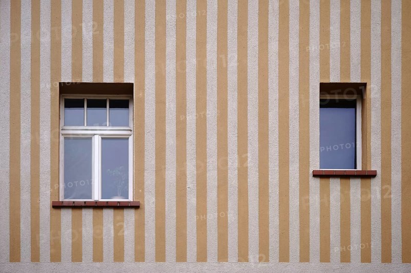 A house wall with a yellow and beige striped wall painting with two windows