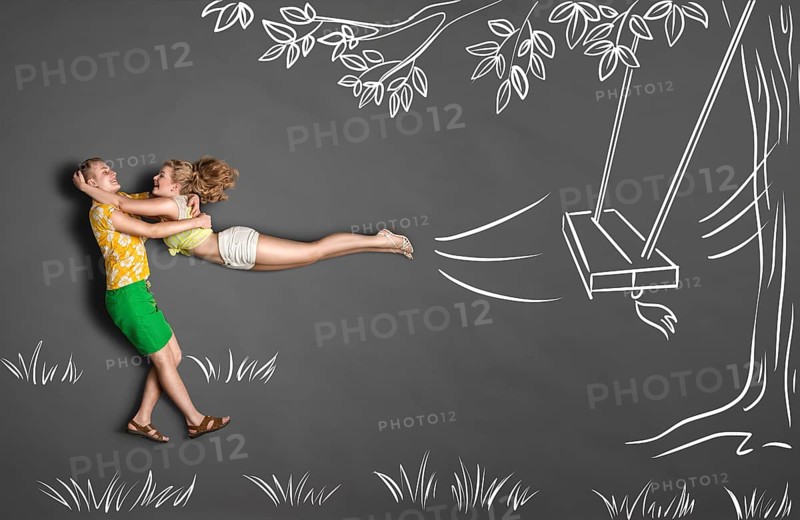 Happy Valentine's Day love story concept of a romantic couple against chalk drawings background. Male catches his girlfriend jumping from tree swinging