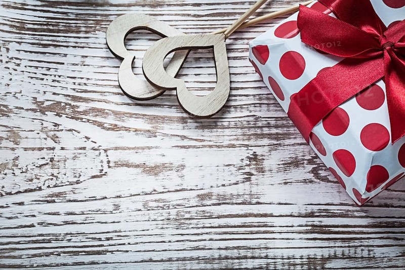 Present box with tied red bow wood hearts on vintage wooden board holidays concept