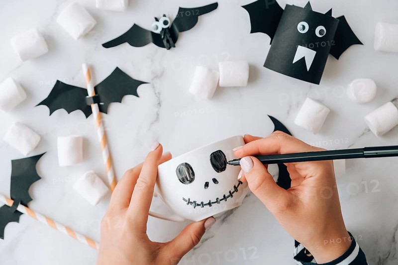 Female hands paint on white cup scary jacks face DIY for kids Halloween home activities Holiday art children craft Handmade decorations. Step by step Socially distanced at home Idea for art class