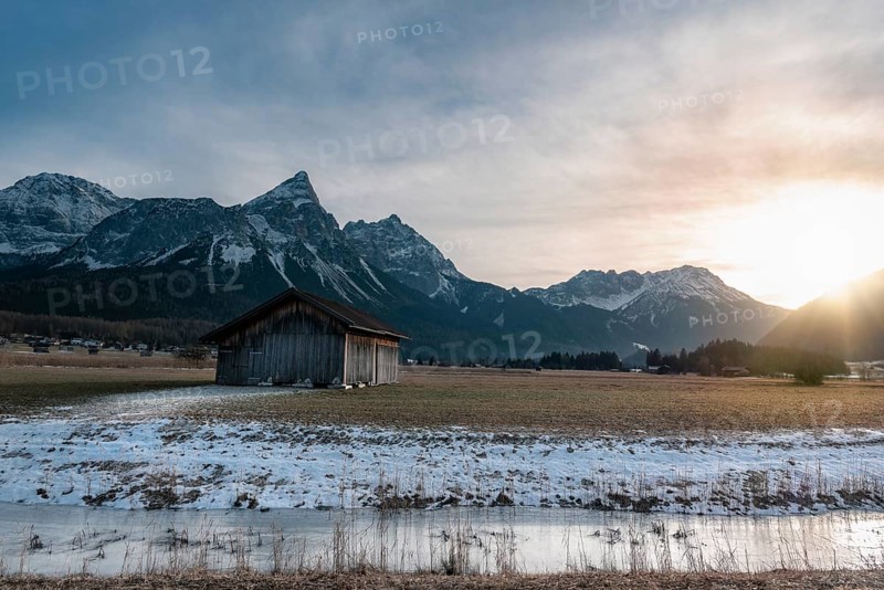 Winter alpine landscape with a wooden cabin, a frozen river and the snowy Alps mountains at sunset, near Ehrwald, Austria, Europe