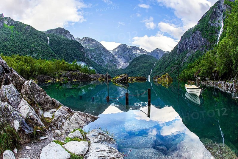 The boat is reflected in the clear water of the lake. Gorgeous Norway. Emerald green of summer grass. The mountain lake Bondhuswatnet. The picture was taken with a fisheye lens