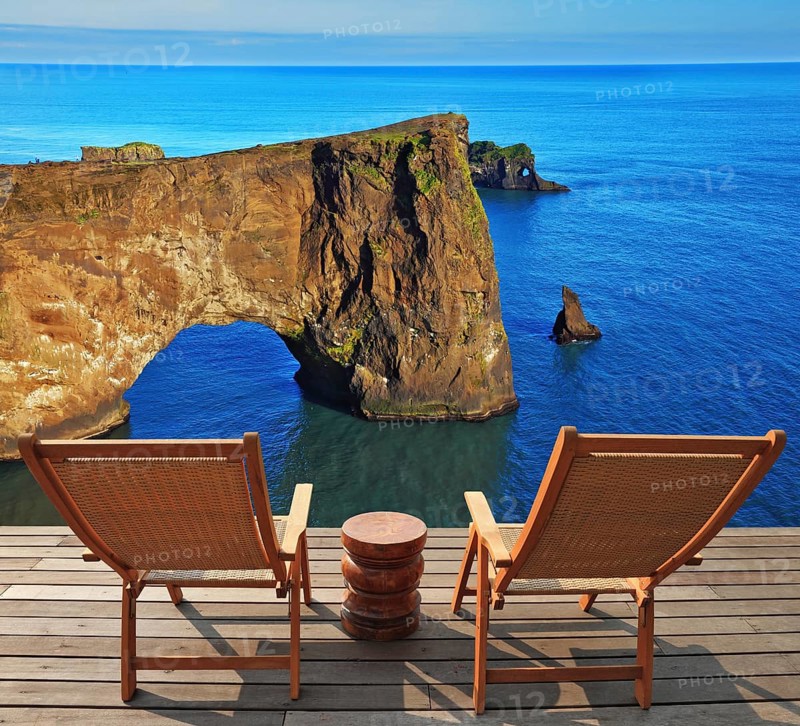 Cape Dirholaey in southern Iceland in July. The colossal rock lit summer sunset. On a coastal rock delivered comfortable wooden loungers