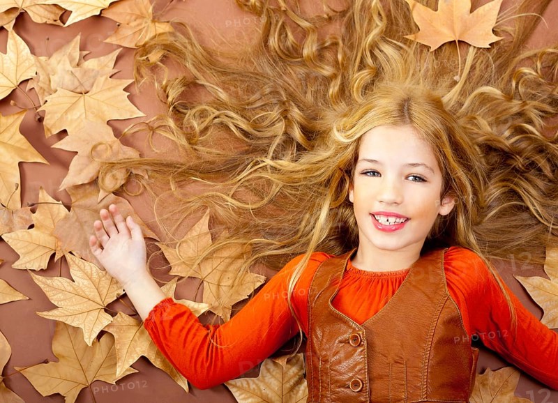 Autumn fall little blond girl on dried tree leaves background and long spread hair
