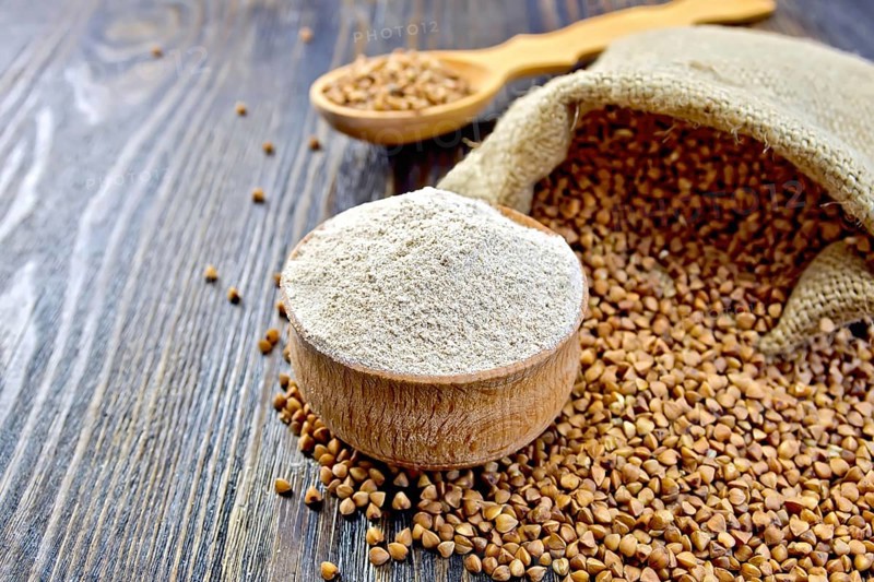 Buckwheat flour in a wooden bowl, buckwheat in a bag on a wooden boards background