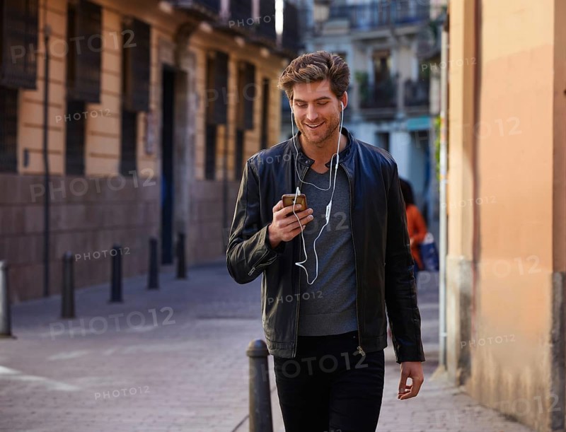 Young man listening music with smartphone earphones walking in the street