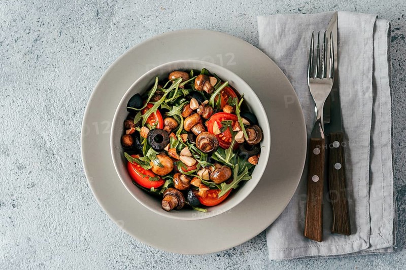 Salad with arugula, mini champignons, cherry tomatoes, black olives, pine nuts. Vegetarian salad top view or flat lay. Copy space. Horizontal banner
