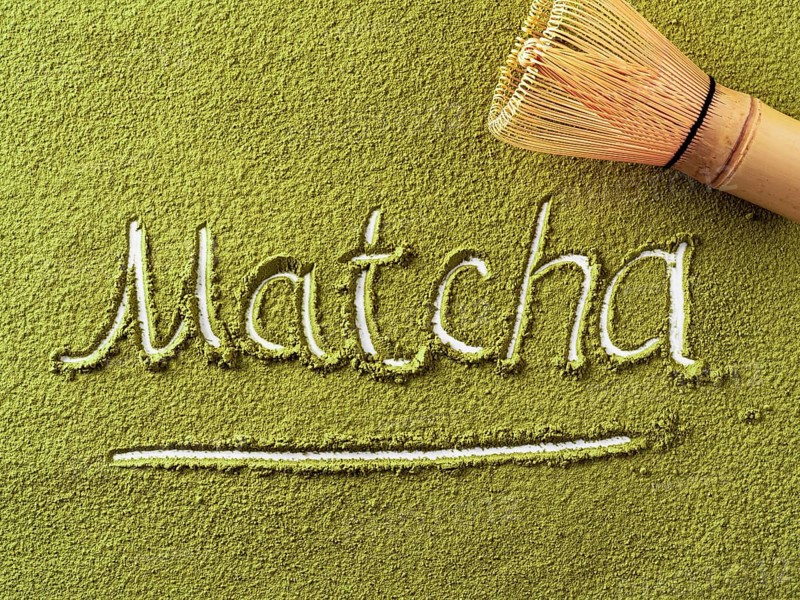 Matcha word over green matcha tea powder background and bamboo whisk Chasen. Top down view or flat lay