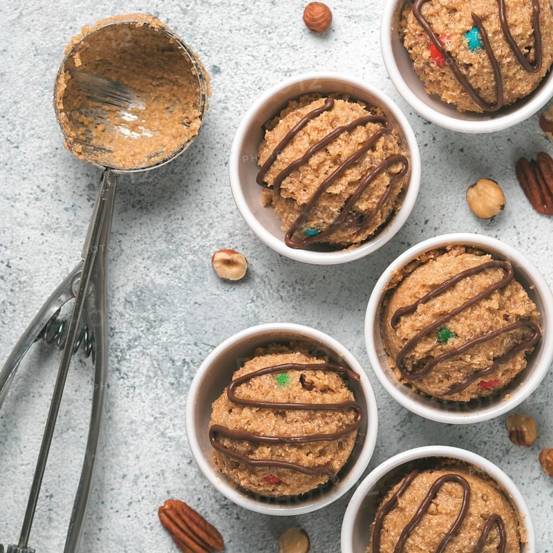 Safe-to-eat raw monster cookie dough in small portion bowl, ice cream scoop and nuts on gray cement background. Ideas and recipes for kids and toddlers meal. Top view or flat-lay
