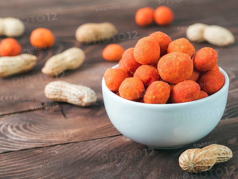 Peanut snack for beer, wine, party bar. Salted peanuts in red spicy chilli glaze on brown wooden table. Copy space