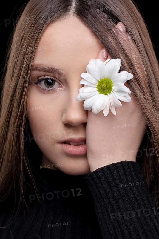 A beautiful girl with natural beauty holds a white flower near her eye. Young girl with a white chrysanthemum