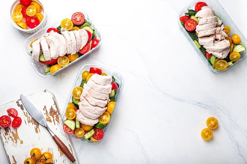 Healthy meal prep for lunch, diet boiled chicken fillet with vegetables salad in lunch boxes containers top view on white marble kitchen table background with knife and cutting board. Space for text, food photography, food photography