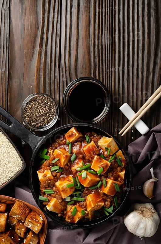 Mapo tofu in cast iron skillet with pork chopped chives soy sauce sichuan pepper garlic and spices closeup on wooden table. Flat lay