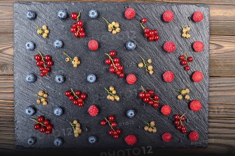 Flat lay view at ripe bilberry raspberry white and red currant on slate stone tray closeup