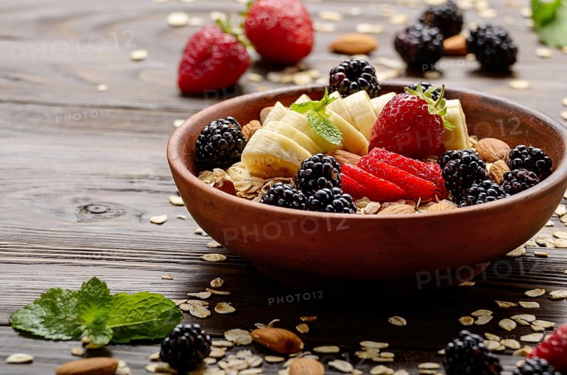 Fruit healthy muesli with banana strawberry almonds and blackberry in clay dish on wooden kitchen table