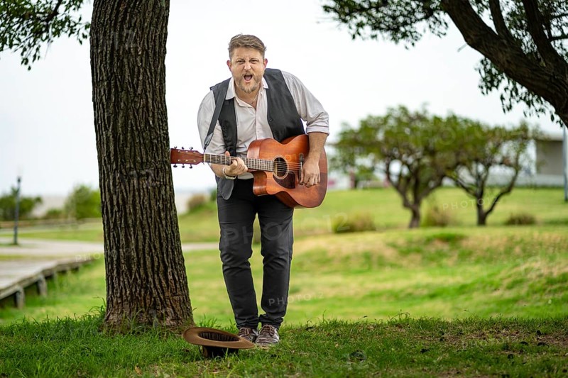 Musician looking at camera while playing guitar and singing in a park