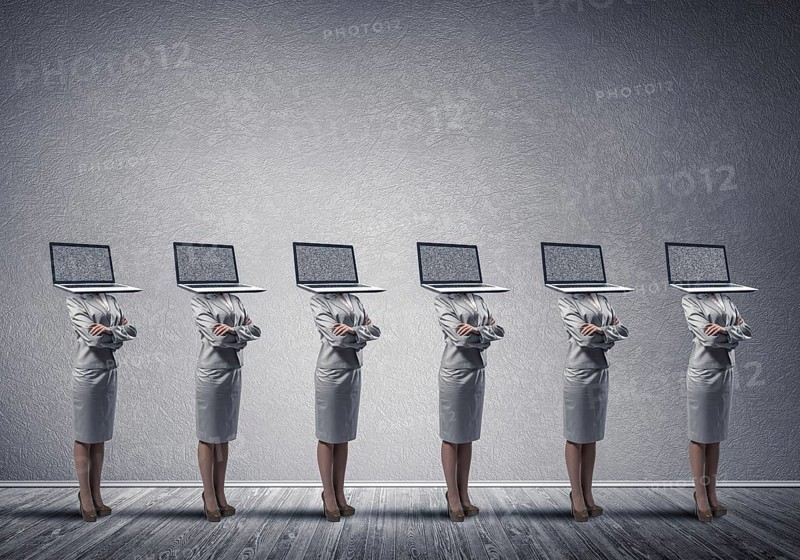 Business women in suits with laptop instead of their heads keeping arms crossed while standing in a row in empty room with gray wall on background
