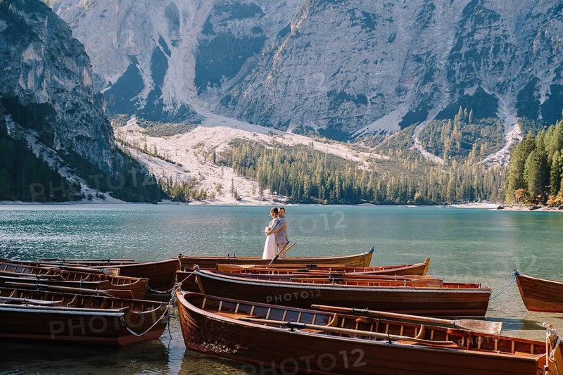 Bride and groom sailing in wooden boat, with oars at Lago di Braies lake in Italy. Wedding in Europe - Newlyweds are standing embracing in a boat