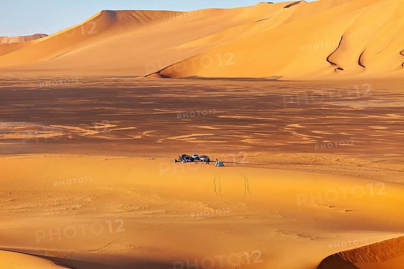 Wide sand dune landscape in yellow tones, with a small camp in the middle of the dunes, tent camp in the endless sand and dune landscape in the Sahara in Algeria