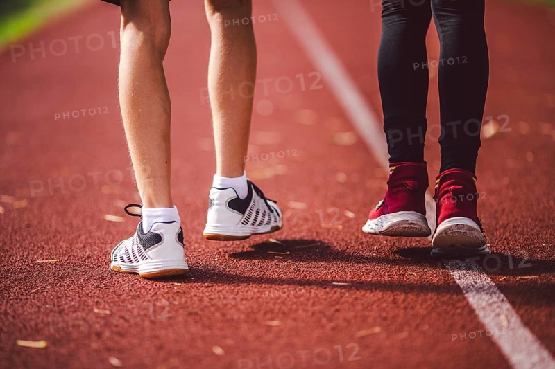 Subject is sport, physical development, sports training for school children in education. Close-up of legs of two children boy and girl running across red running stadium, back view