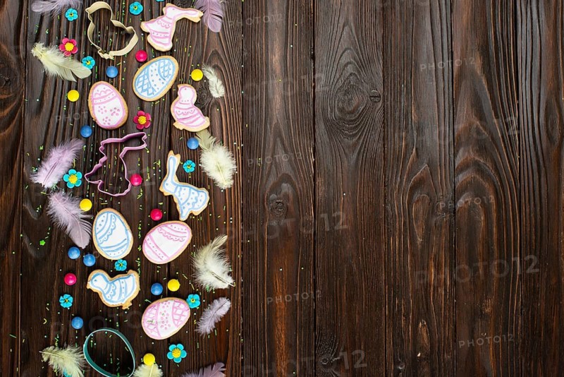 Sugar sprinkles, candies, feathers, cookie cutters, Easter frosted cookies in shape of egg chicken and rabbit on wooden table background. Flat lay mockup with copy space