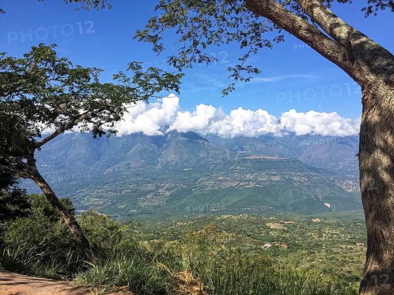 Tree framed view into a green valley and mountains with white clouds and blue sky, Barichara, Colombia, South America
