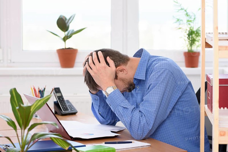 Office employee clutching his head in his hands while reading a document