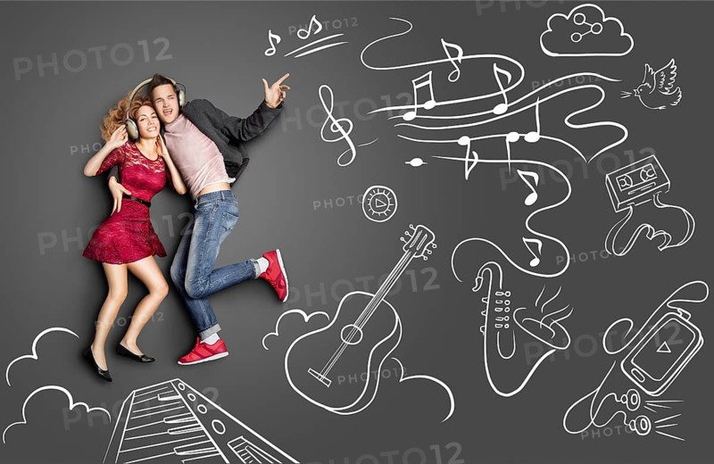Happy valentines love story concept of a romantic couple sharing headphones and listening to the music against chalk drawings background of musical instruments