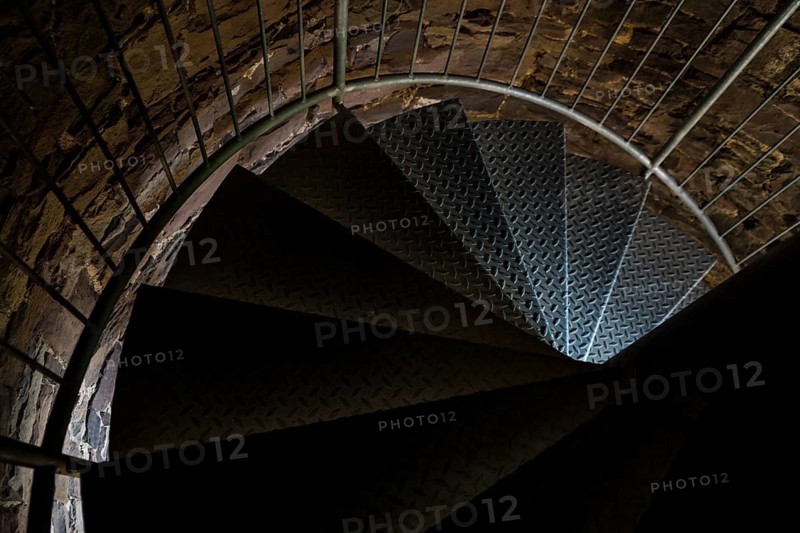 Steps of old metal spiral staircase disappear in darkness