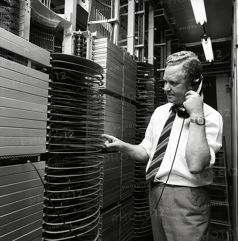 Telephony in the 1970s. A man in a room with an automatic switchboard connecting the calls through a mechanical device that connected the calling and receiving parts. The manufacturer is LM Ericsson. Sweden 1971 Kristoffersson ref ED