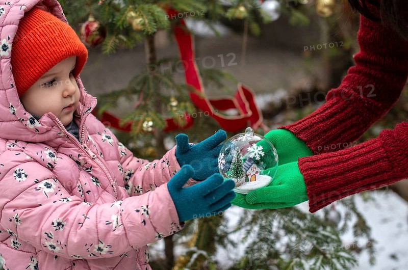 Crystal christmas ball with house and snow inside. Hands with green gloves gives transparent ball to a child