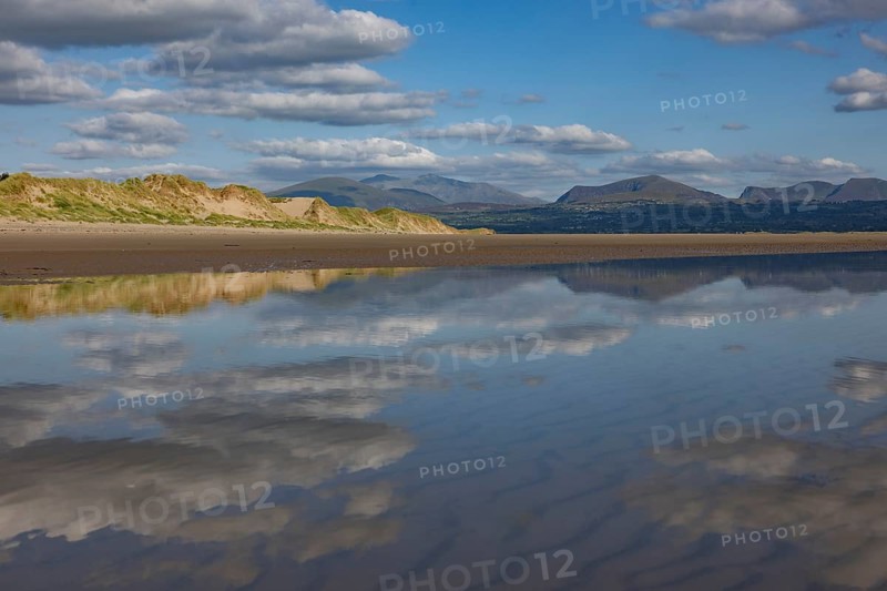 Reflection of clouds and mountains of Snowdonia National Park in the water on the beach, Newborough, Anglesey, Wales, Great Britain