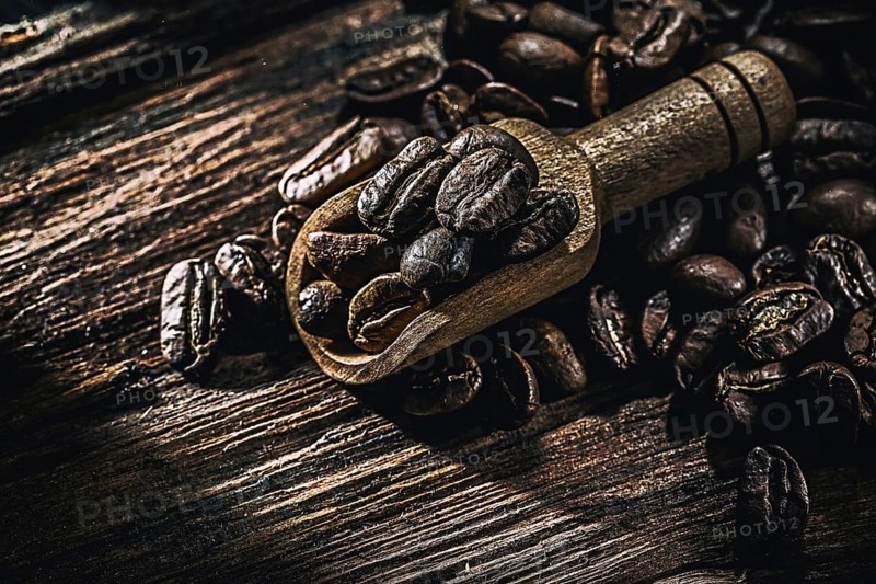 Wholegrain coffee seeds in scoop on wooden board