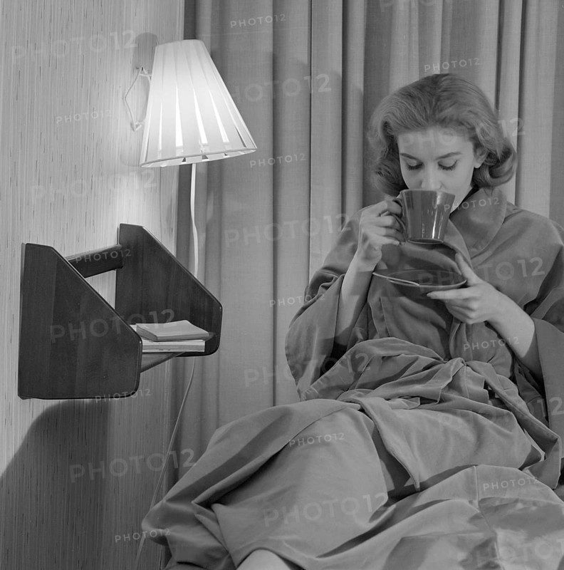 Teatime in the 1950s. A young woman in an evening gown sits comfortably and drinks a cup of tea. Sweden 1950s