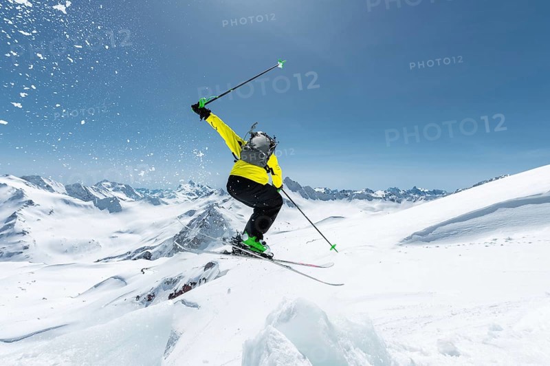 A skier in full sports equipment jumps into the abyss from the top of the glacier against the background of the blue sky and the Caucasian snow-capped mountains. View from the back. Elbrus region. Russia