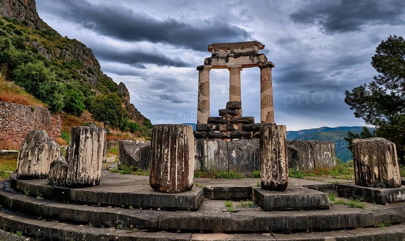 Ruins of Tholos of ancient Greek goddess Athena Pronaia in Delphi, Greece. Three Doric columns with relieves on frieze of circular temple on slope of sacred mount Parnassos and next to famous Delphi complex. UNESCO World heritage site. Rear view