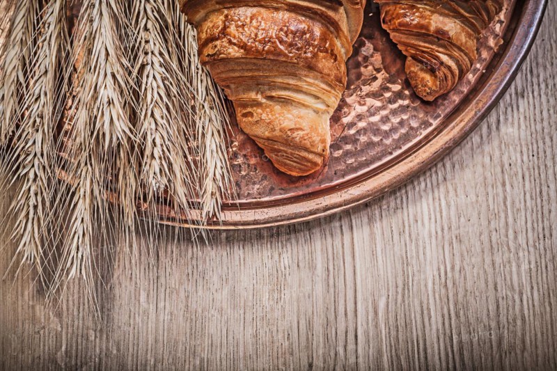 Composition of wheat rye ears freshly baked croissants Copper tray on wooden board