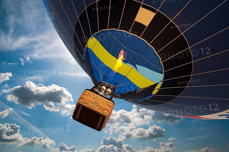 Hot air balloon with gondola in front of a blue sky with white clouds