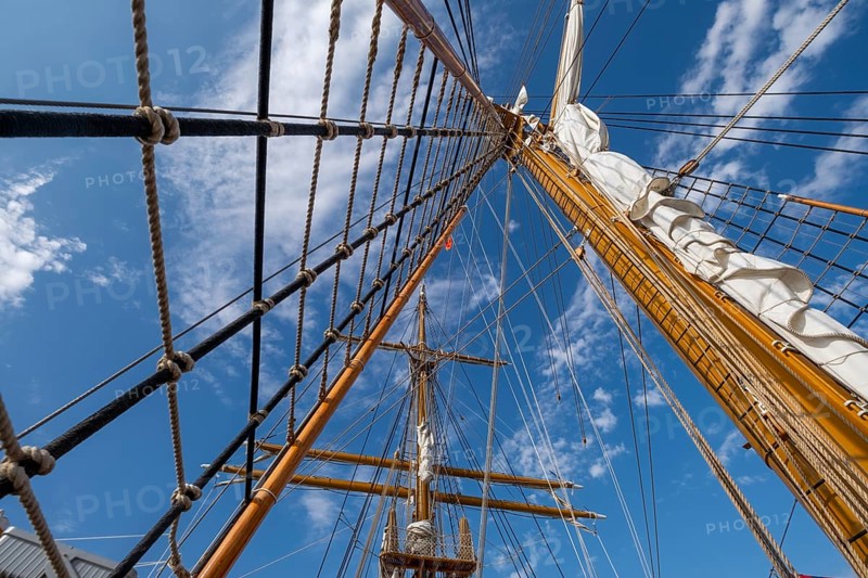 Low angle view of sailboat wooden ship masts and rigging under blue sky with clouds