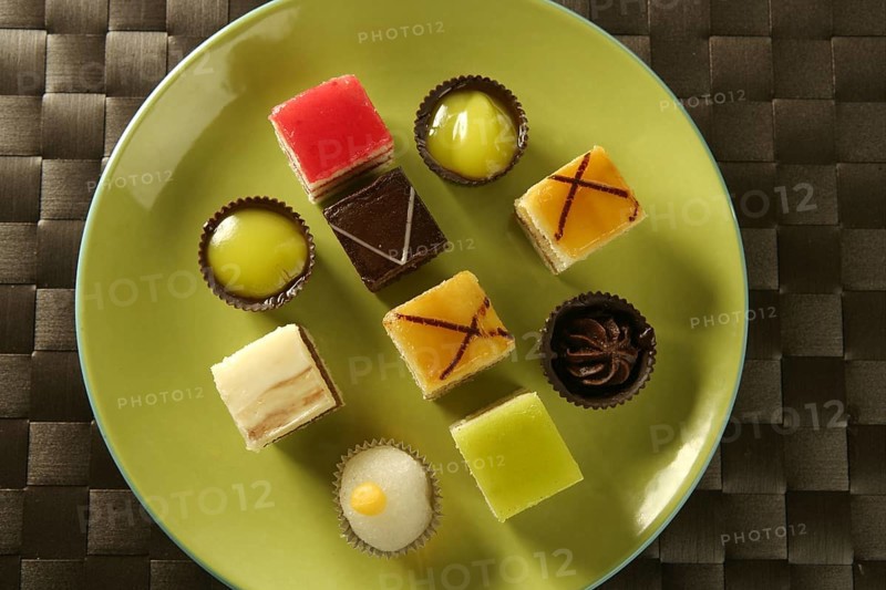 Varied pastries in green dish. Little colorful cakes