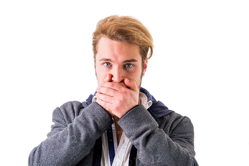Young blond man covering his mouth while looking at camera against of white background