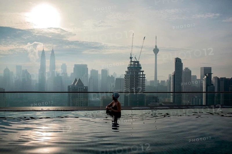Woman enjoying cityscape of Kuala Lumpur from rooftop swimming pool. Urban scene with skyscrapers, Petronas Tower and Kuala Lumpur Tower, Malaysia, Asia