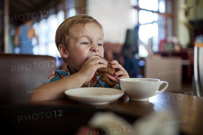 Little boy in a cafe eating big tasty sandwich. Hungry child