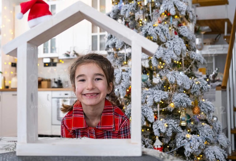 Happy child with tiny house in cozy home with Christmas decor of festive white kitchen. Gift for New Year. Insurance, moving to new house, mortgage, rent and purchase real estate